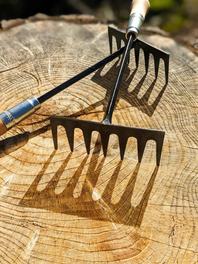 Hand Rake hand forged by Homestead Iron on wooden background with deep shadows. 