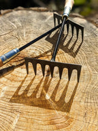 Hand Rake hand forged by Homestead Iron on wooden background with deep shadows. 