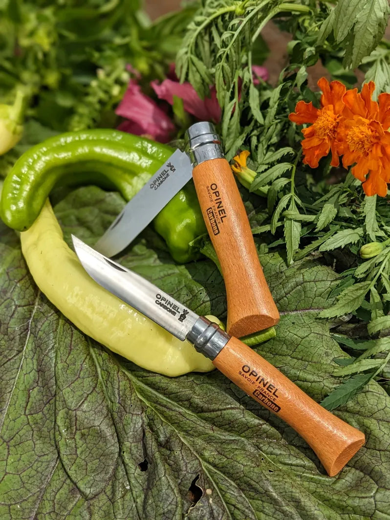 Two Opinel pocket knives on a leafy background with flowers